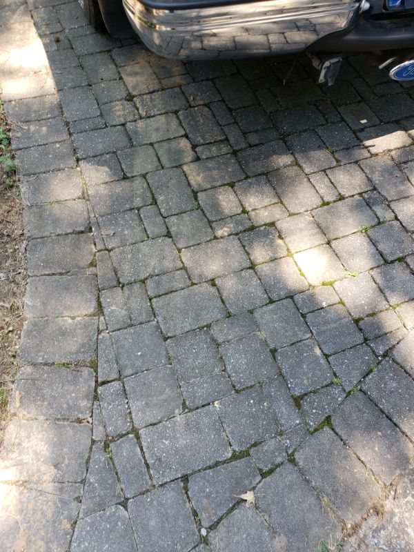 Paver stone driveway with interlocking gray bricks, landscaping rocks, and moss growth, showcasing landscape design and hardscape installation.