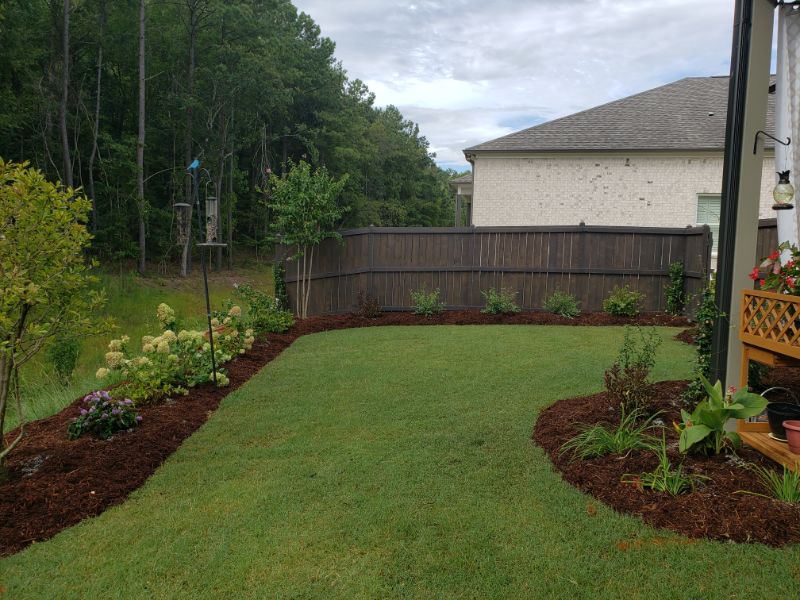 Lush backyard landscape design with well-maintained lawn, colorful flowering plants, and garden beds, showcasing professional landscape architecture services by John Russell Landscape Architect.