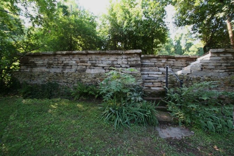 Stone retaining wall with lush garden plants in a landscaped yard, showcasing expert landscape architecture and hardscape design.