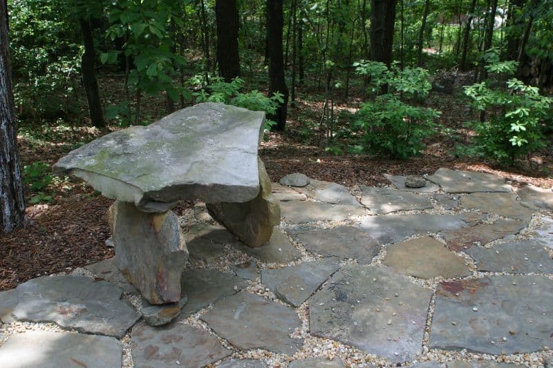 Natural stone patio with rustic bench in wooded landscape by John Russell Landscape Architect.