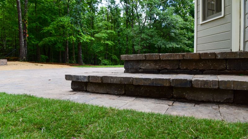 Natural stone patio with layered brick steps in a landscaped yard, designed by John Russell Landscape Architect, blending outdoor living space with surrounding greenery and trees.