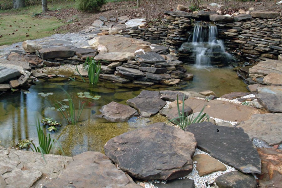 Natural stone water feature with waterfall, pond, and aquatic plants, designed by John Russell Landscape Architect for outdoor landscape and garden pond design.