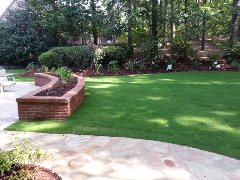 Lush green lawn with brick garden bed, landscaped backyard by John Russell Landscape Architect, showcasing professional landscape design and garden maintenance services.