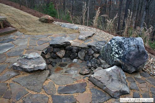 Natural stone fire pit with large rocks and flagstone patio, landscape design by John Russell Landscape Architect. Perfect for outdoor gatherings and backyard enhancements.