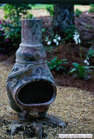 Vase garden sculpture with intricate patterns, surrounded by lush greenery and blooming flowers in a landscaped outdoor space.