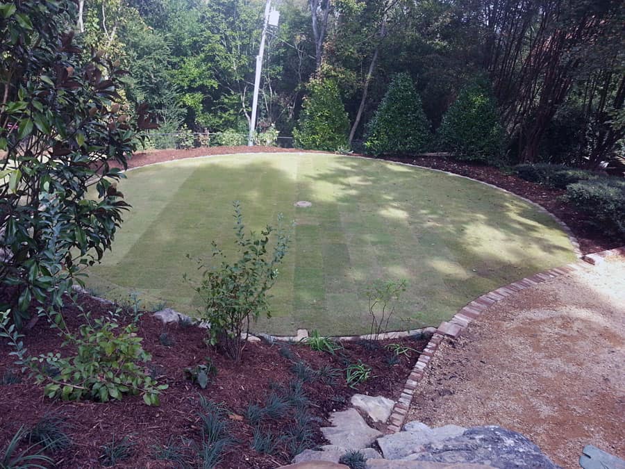 Lush landscape design with a well-manicured lawn, surrounded by mature trees and shrubs in a tranquil outdoor garden setting.