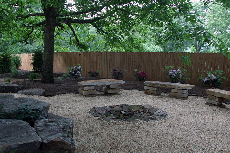 Natural outdoor backyard fire pit area with stone benches and lush greenery, designed by John Russell Landscape Architect.