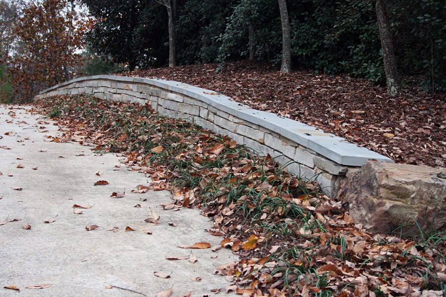 Natural stone retaining wall with fallen autumn leaves and lush landscape plants, designed by John Russell Landscape Architect, enhancing garden durability and aesthetic appeal.