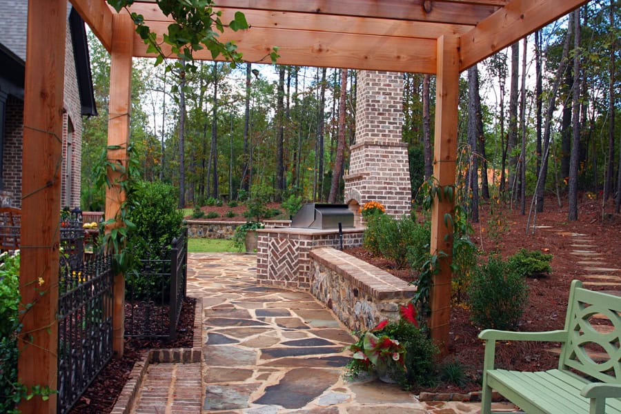 Modern outdoor living space with stone patio, built-in grill, and lush landscaping by John Russell Landscape Architect.