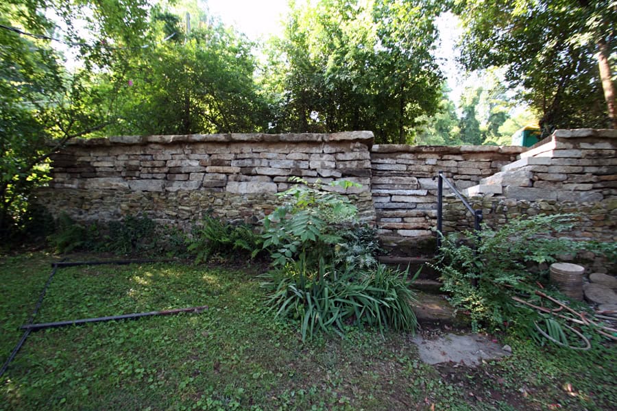 Natural stone retaining wall with lush green foliage surrounding a landscaped garden area.