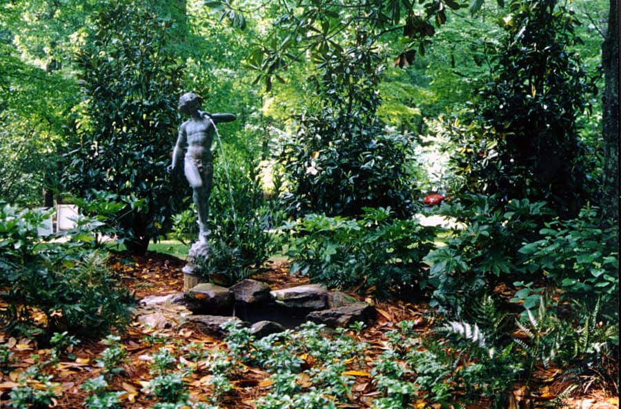 Stone statue of boy with water fountain surrounded by lush greenery in a landscape garden.
