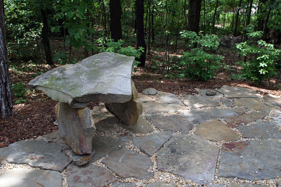Natural stone outdoor seating area with rustic rock bench in lush garden setting.