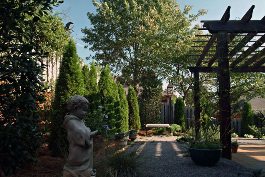 A lush garden landscape designed by John Russell Landscape Architect featuring elegant trees, a decorative pergola, sculptures, and vibrant greenery creating a tranquil outdoor space.