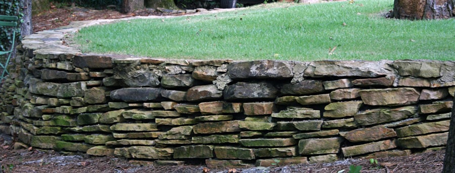 Stone retaining wall with layered natural stone, landscaping by John Russell Landscape Architect in a lush garden setting.