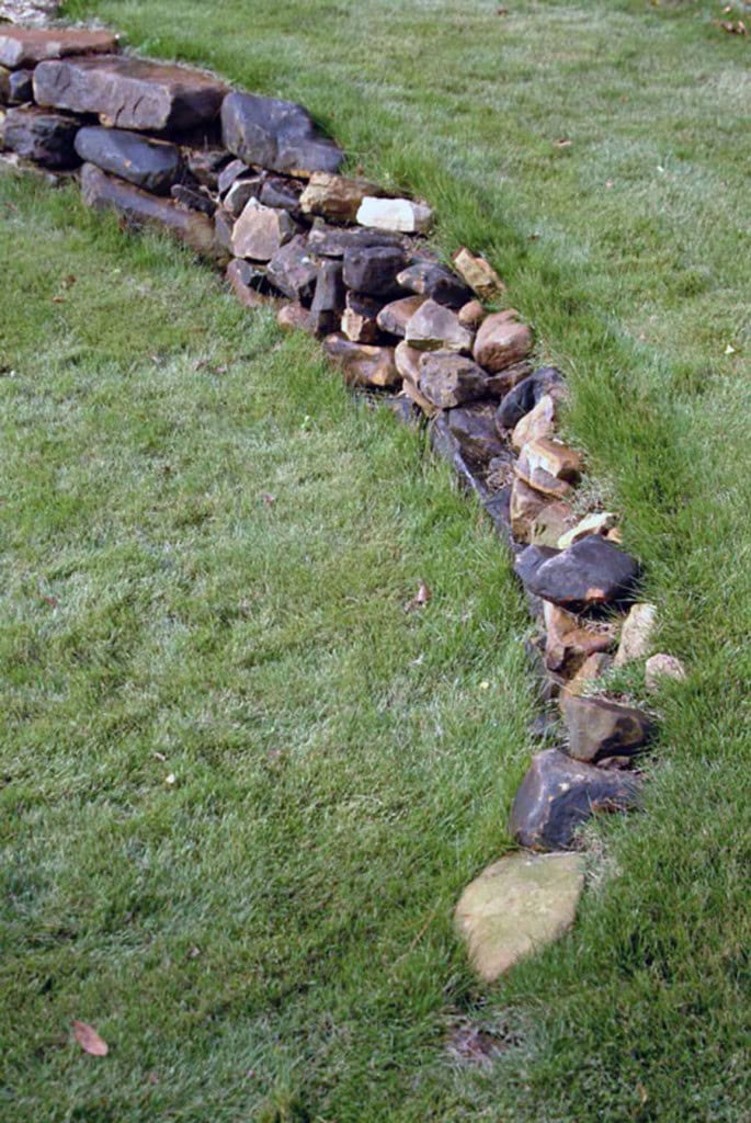 Natural stone garden edging using stacked rocks on lush green lawn.