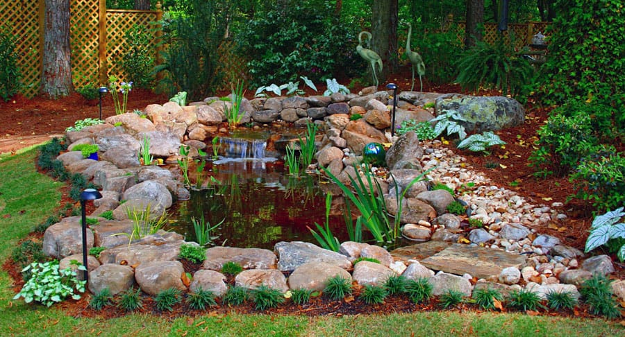 Lush landscape garden with pond, rocks, and greenery, designed by John Russell Landscape Architect. Perfect outdoor space for relaxing and enjoying nature. High-quality landscape design services.