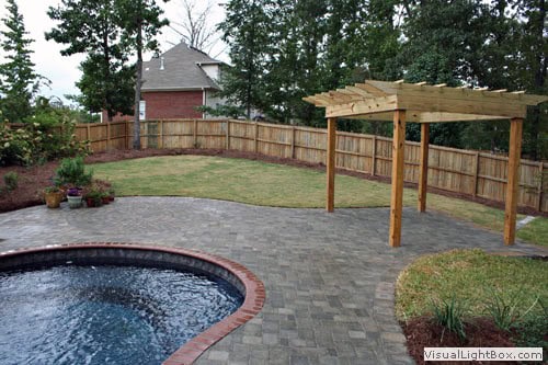 Natural backyard patio with pergola, paver walkway, lush lawn, and privacy wooden fence, creating a beautiful outdoor living space.