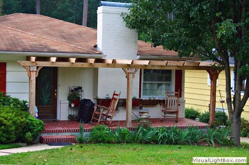 Rustic front porch with wooden pergola, lush greenery, and garden beds, showcasing John Russell Landscape Architect's residential landscape design expertise.