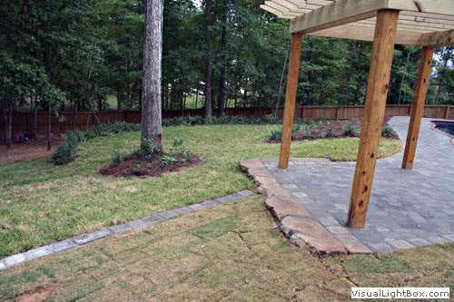 Lush backyard landscape design with a wooden pergola, stone patio, and manicured lawn showcasing professional landscape architecture services.