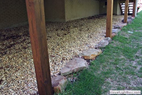 Natural stone landscape edging with gravel and wooden supports in a backyard garden.