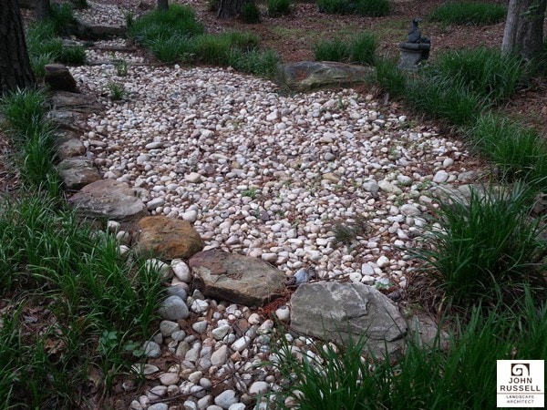 Natural stone dry creek bed in landscaped backyard, crafted by John Russell Landscape Architect, showcasing expert landscape design and sustainable outdoor spaces.