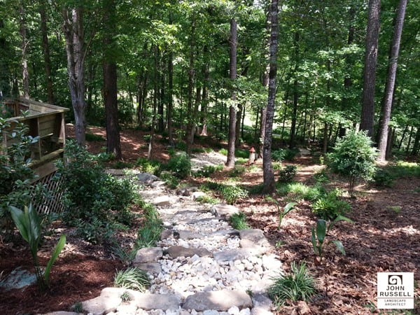 Natural woodland garden with stone pathway, lush greenery, and mature trees, designed for outdoor relaxation and landscape aesthetics by John Russell Landscape Architect.