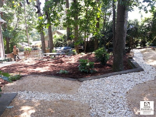 Lush backyard landscape design with gravel pathways, mature trees, and shrubbery by John Russell Landscape Architect for a natural and inviting outdoor space.