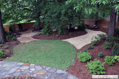 Lush landscaped backyard with winding stone pathways, vibrant green lawn, and mature trees, designed by John Russell Landscape Architect.