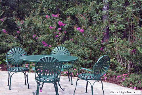 Elegant outdoor patio with turquoise metal table and chairs surrounded by lush flowering bushes and greenery, perfect for relaxing garden spaces and landscape design.
