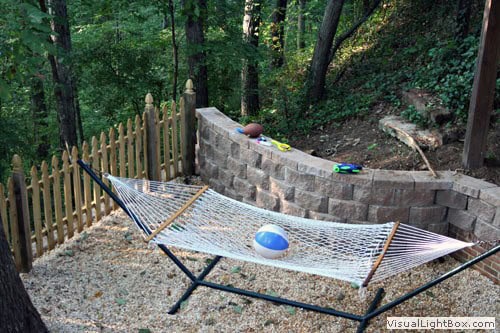 A playful backyard hammock area with a stone retaining wall, surrounded by lush trees and greenery, perfect for relaxation and outdoor enjoyment.