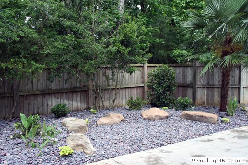 Large backyard landscape design with rocks and lush greenery, showcasing professional landscape architecture services by John Russell.