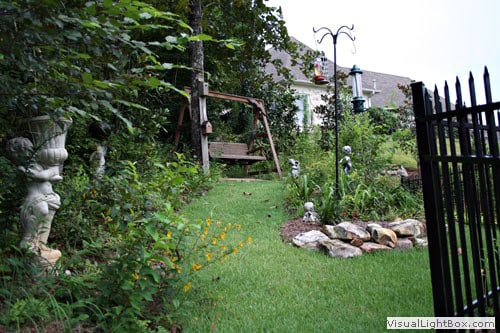 Lush backyard garden landscape design featuring a wooden bench, decorative statues, and vibrant flowers, crafted by John Russell Landscape Architect.