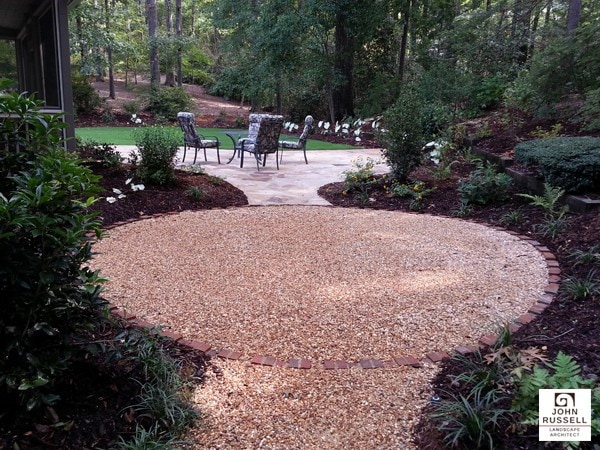 Crushed gravel circular patio with surrounding lush garden landscape and outdoor seating area.