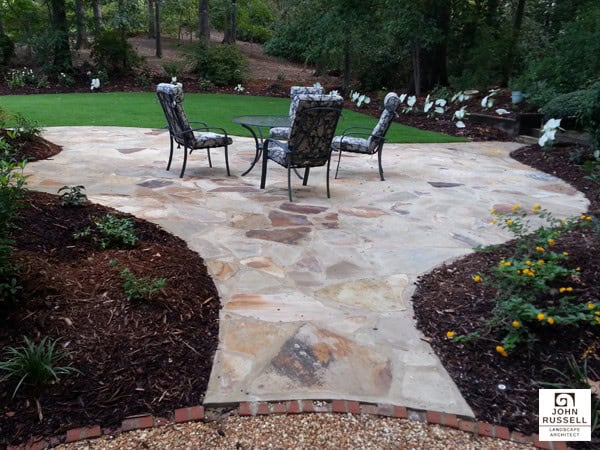 Natural flagstone patio with decorative garden beds and outdoor seating, expertly designed by John Russell Landscape Architect for elegant backyard landscapes.