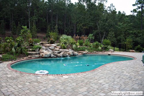 Pool design with natural stone waterfall, surrounded by lush landscaping and a paver patio, created by John Russell Landscape Architect.