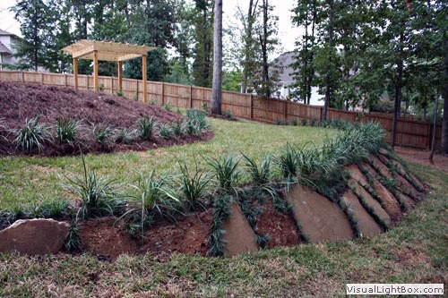 Lush backyard landscaping with tiered flower beds, mature trees, and a privacy fence, designed by John Russell Landscape Architect, highlighting expert outdoor space planning and garden design.