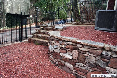 Heavy-duty stone retaining wall with layered landscaping, perfect for gardens and outdoor spaces, designed by John Russell Landscape Architect.