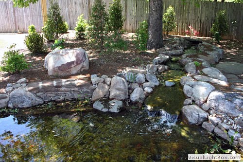 Natural stone water feature with pond and rock garden in a landscaped backyard, designed by John Russell Landscape Architect.