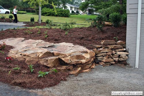 Natural stone retaining wall in a landscaped yard, designed by John Russell Landscape Architect, showcasing expert landscape design and durable rockwork.