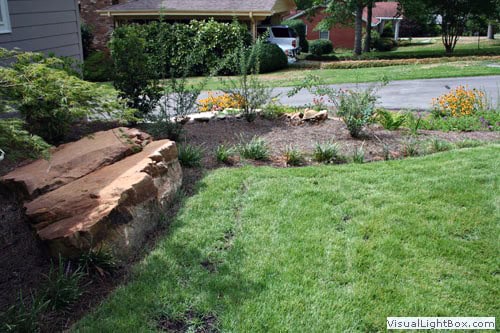 Rocks and landscaped garden bed with lush grass in a professional residential yard design by John Russell Landscape Architect.