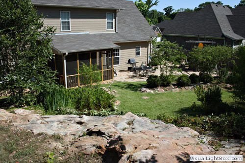 Vibrant backyard landscape design with lush greenery, stone features, and a screened-in porch, showcasing expert landscape architecture by John Russell.
