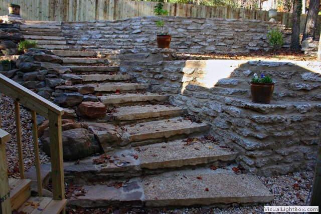 Natural stone landscape stairs with potted plants in a garden setting, designed by John Russell Landscape Architect. Beautiful outdoor landscape architecture emphasizing craftsmanship and aesthetic appeal.