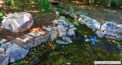Natural stone water feature with cascading stream and lush garden landscape by John Russell Landscape Architect.