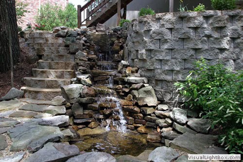 Rock waterfall landscape design with natural stone elements and lush greenery by John Russell Landscape Architect.
