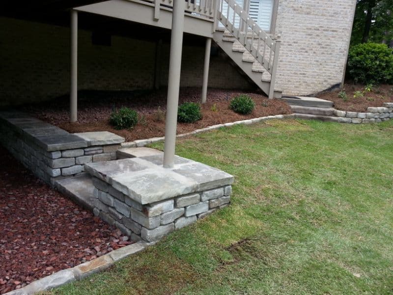 Stone patio with stairs and landscaped garden for outdoor living, designed by John Russell Landscape Architect. Custom stonework enhances backyard aesthetics with functional design.