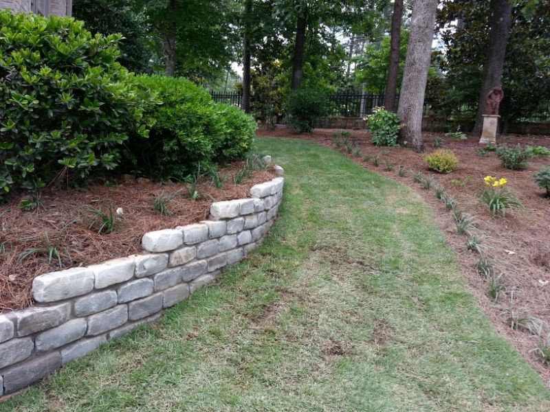 Lush landscaped garden featuring a stone retaining wall, grassy pathway, and diverse plantings, designed by John Russell Landscape Architect for aesthetic appeal and functional outdoor space.