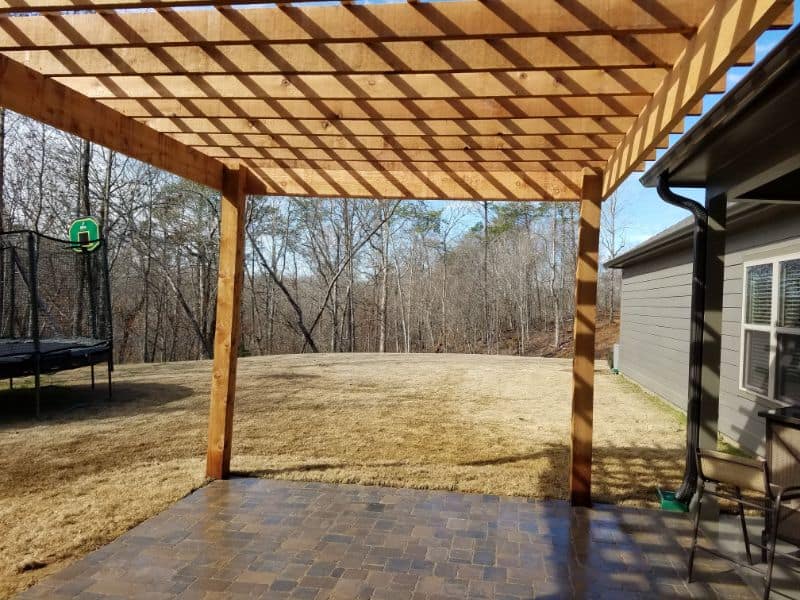 Modern backyard patio with wooden pergola and outdoor seating, landscaped yard, and trampoline, designed by John Russell Landscape Architect, emphasizing outdoor living spaces and landscape design excellence in en_US.
