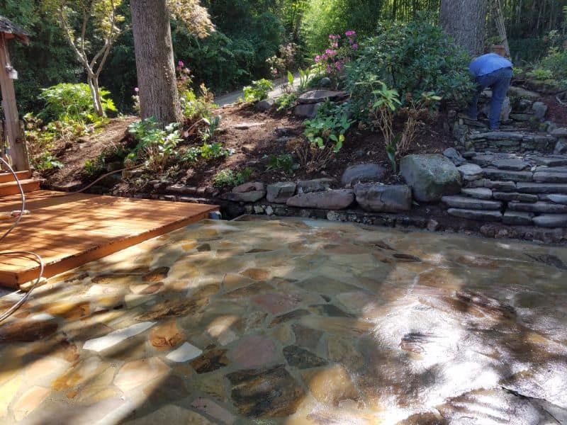 River stone landscaping for serene backyard pond with wooden deck and natural stone steps, designed by John Russell Landscape Architect.