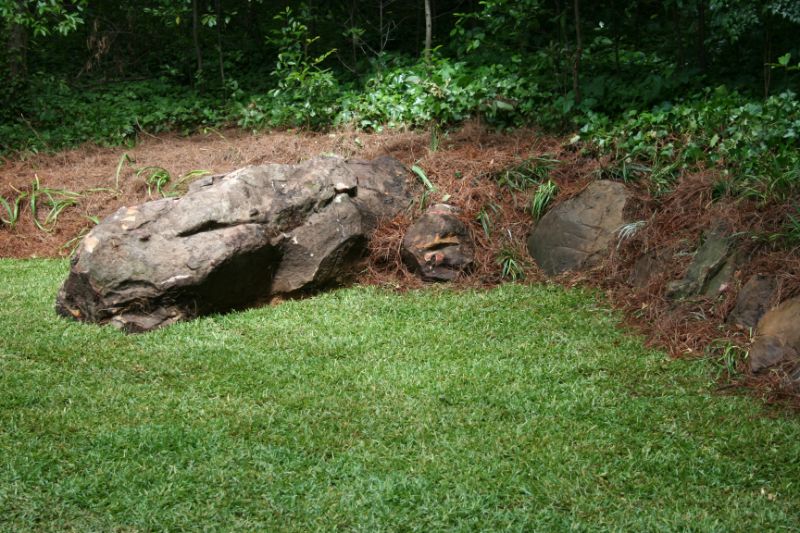 Natural landscape design featuring large decorative rocks and lush greenery by John Russell Landscape Architect, emphasizing landscape architecture and outdoor space excellence.