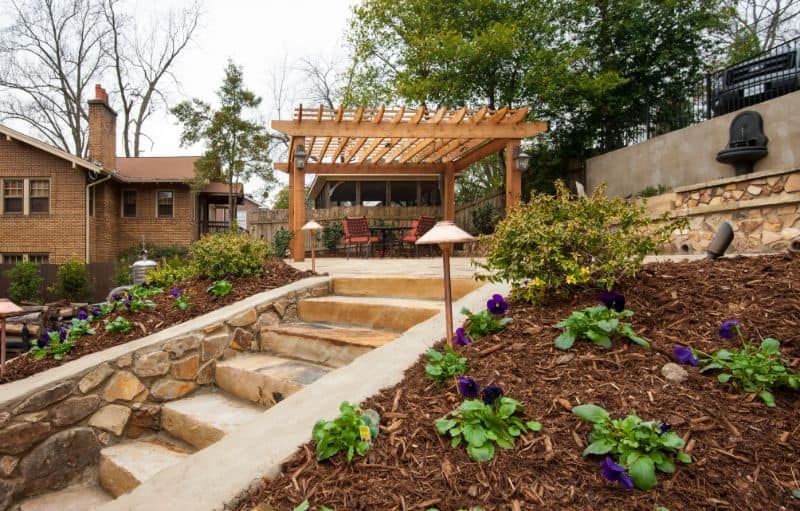 Custom outdoor living space designed by John Russell Landscape Architect, featuring a stone staircase, landscaped garden beds, and a pergola for relaxation and entertainment.
